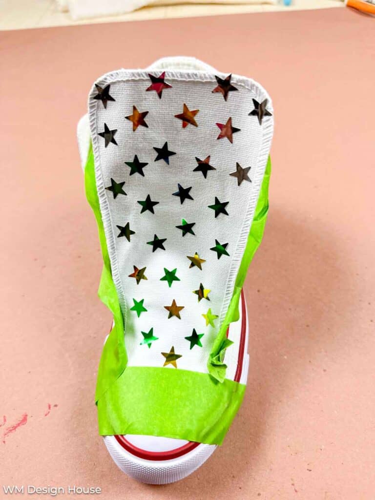 Canvas shoe that is taped off and has star stickers on the tongue in preperation for painting