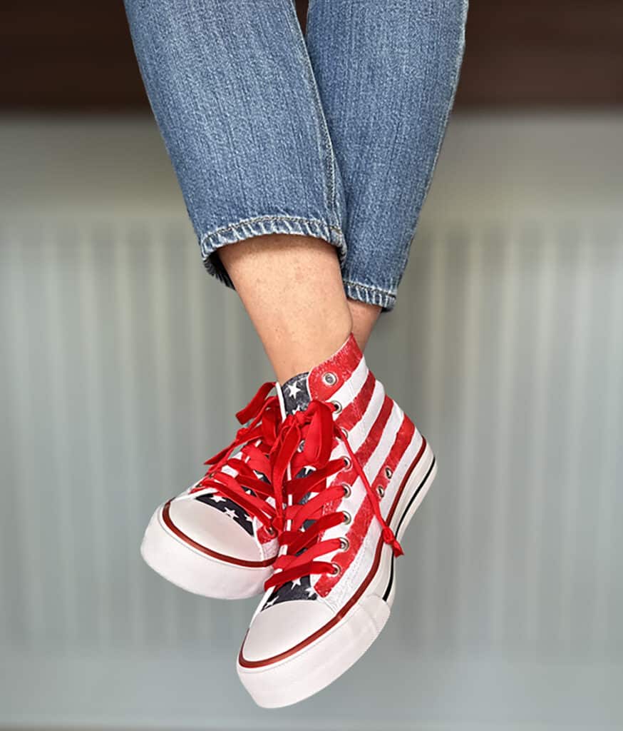 After picture of girls sitting on the counter with her feet hanging off . She is wearing jeans and her patriotic hand painted hight top white tennis shoes. There are stripes on the sides and stars on the tongue with red velvet laces. 