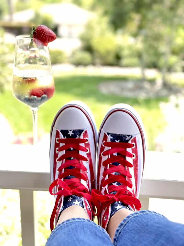 Tennis shoes painted with red stripes on the sides and the tongue is navy blue with white stars. White laces have been replaced with red velvet ribbon