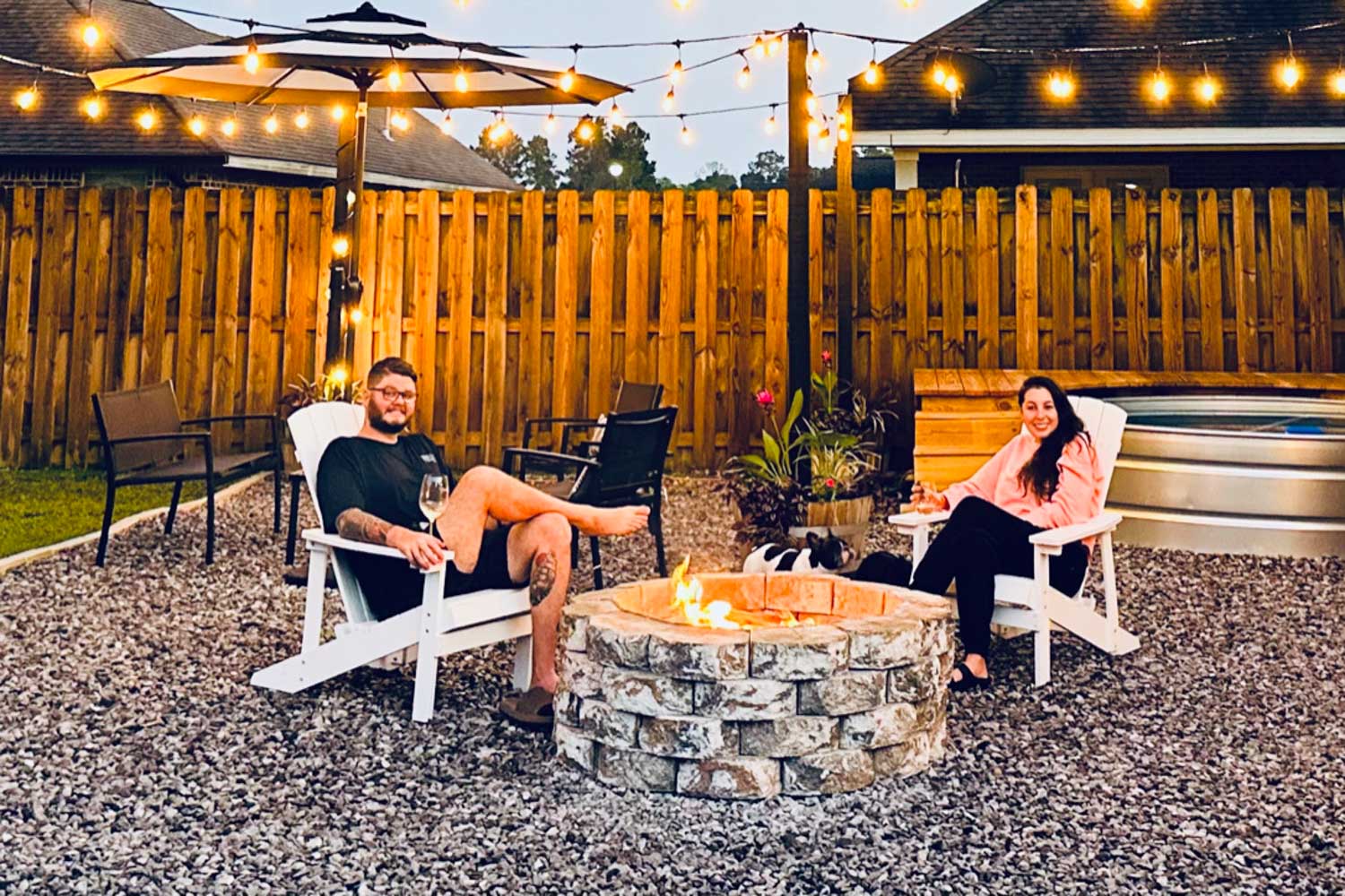 Couple sitting in their new backyard with market lights and fire pit.