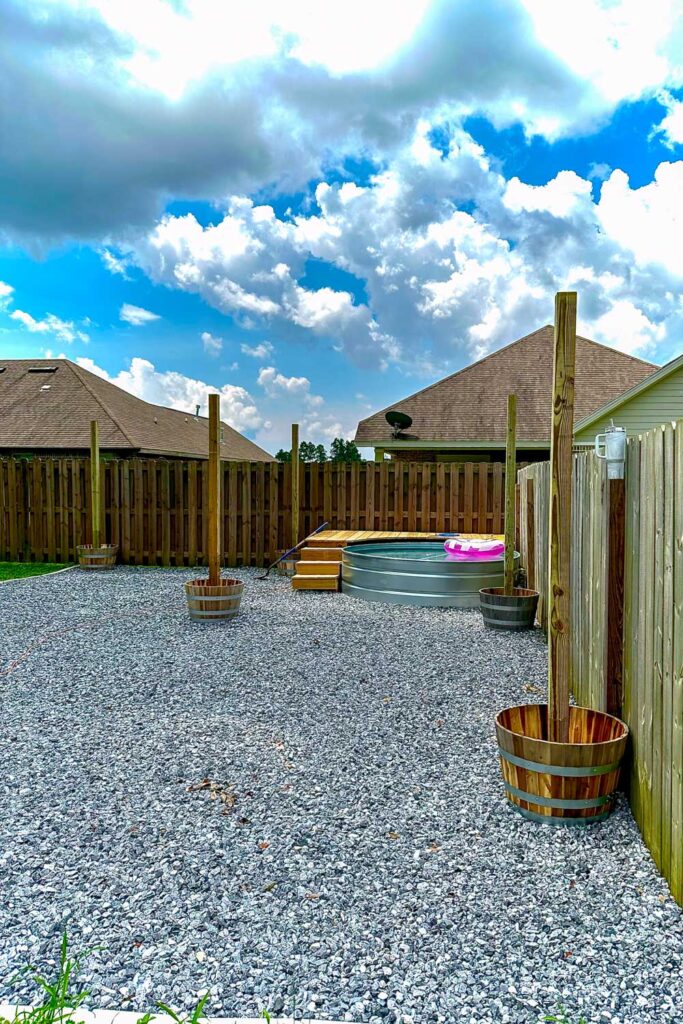 Backyard with a gravel area that contains a stock pool and deck. Wine barrels have been placed where they will stay and are ready for cement. 