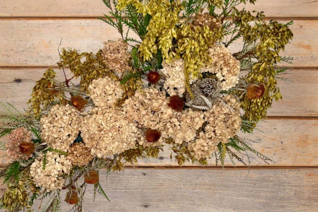 Adding rust colored pincushion dried flowers to a wall foral arrangement