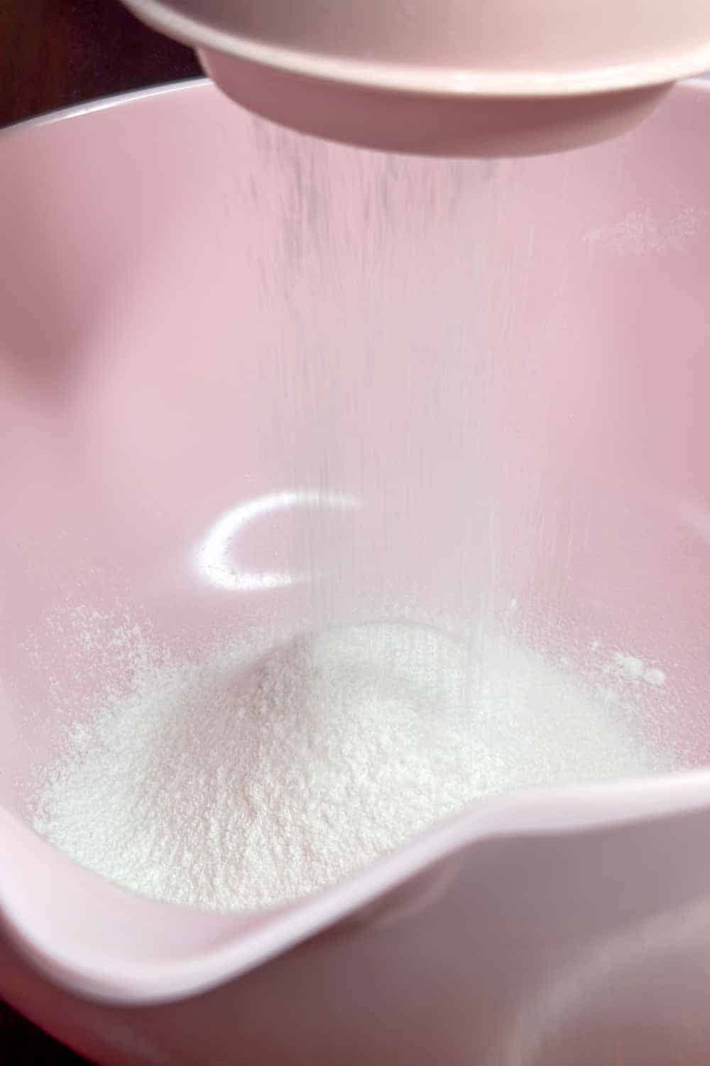 Powdered sugar being sifted into a pink mixing bowl.