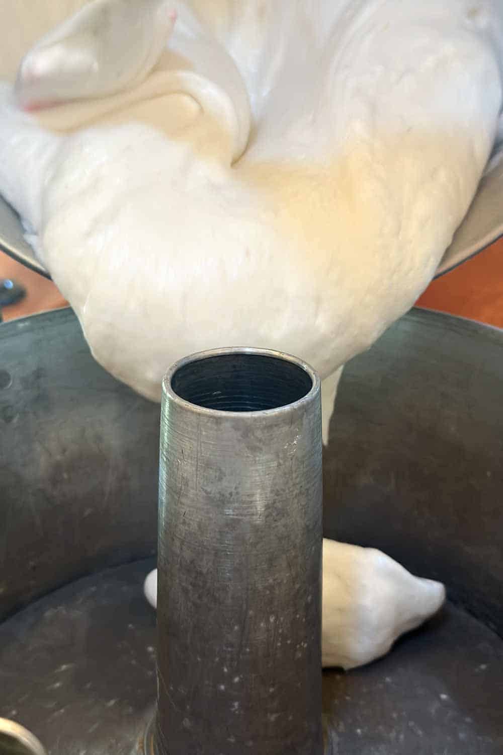Close-up of airy, white batter being poured into a greased tube pan. The batter is fluffy and thick, gently cascading down the sides of the pan's central tube. The setting appears to be a kitchen countertop.