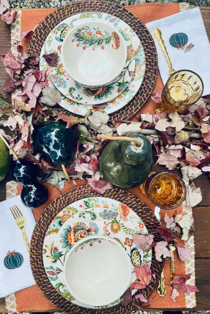 Fall outdoor table with blue gourds and paisley dishes on orange placemats. 