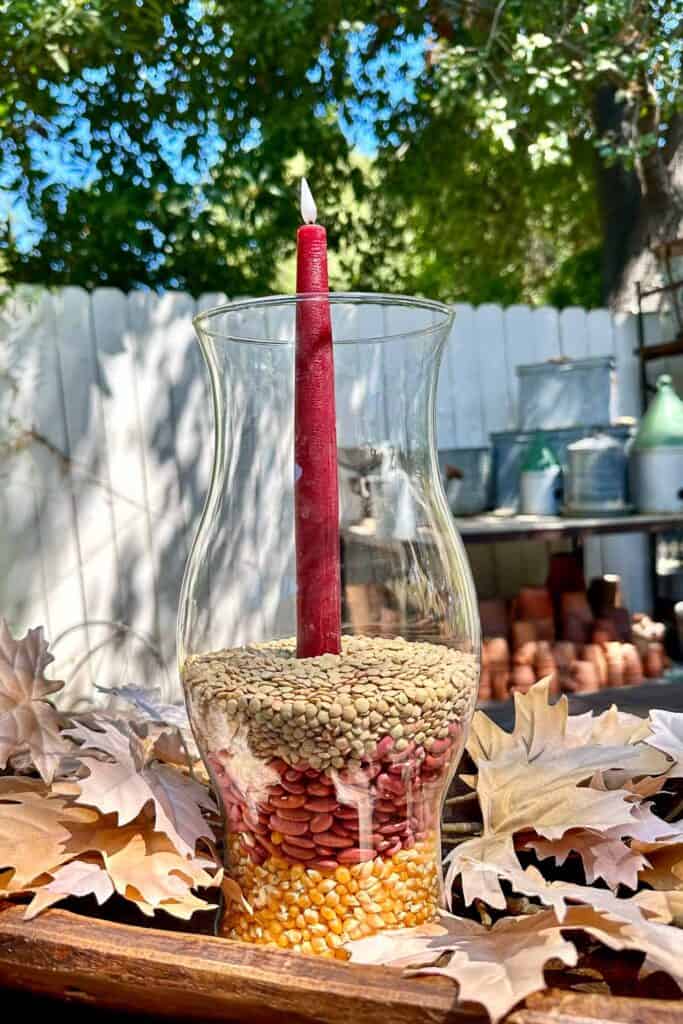 Glass Hurricane filled with popcorn, kidney beans and dried lentils. Holding up a taper candle sitting in a dough bowl. 