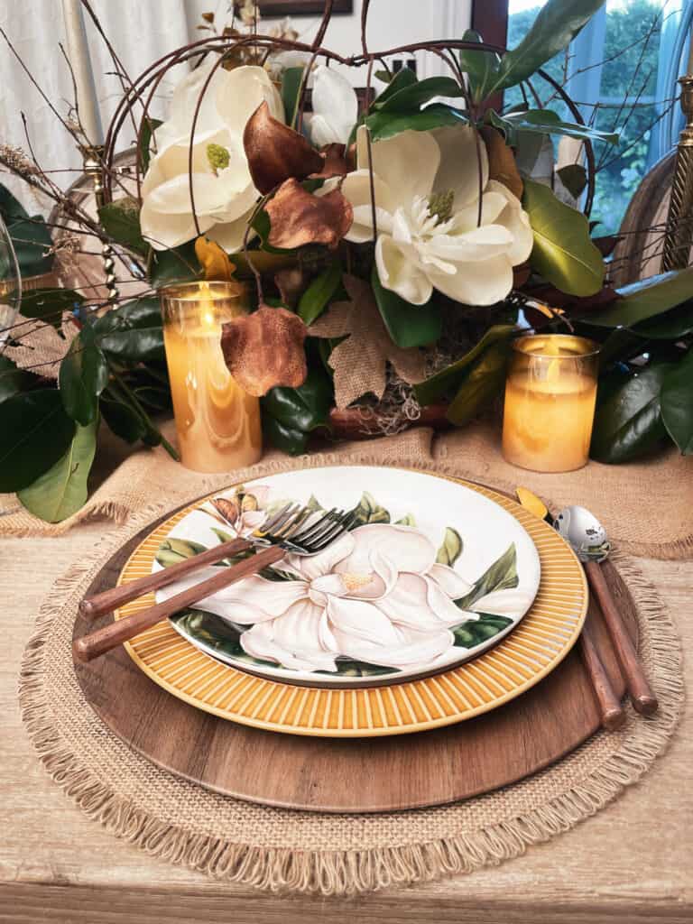 Fall table setting with magnnolia plates and fresh magnolia centerpiece in a pumpkin wire frame 