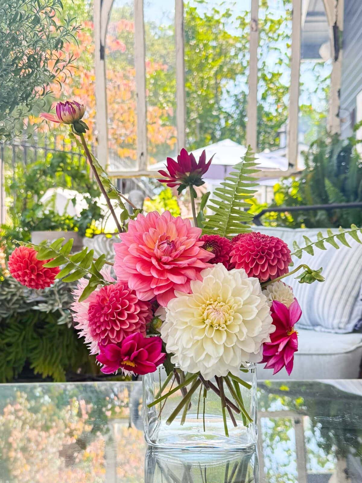 Small dahlia arrangement with Boom Boom White, Jowey Linda, Sweet Nathalie, and Rocco dahlias in a glass vase on a patio table