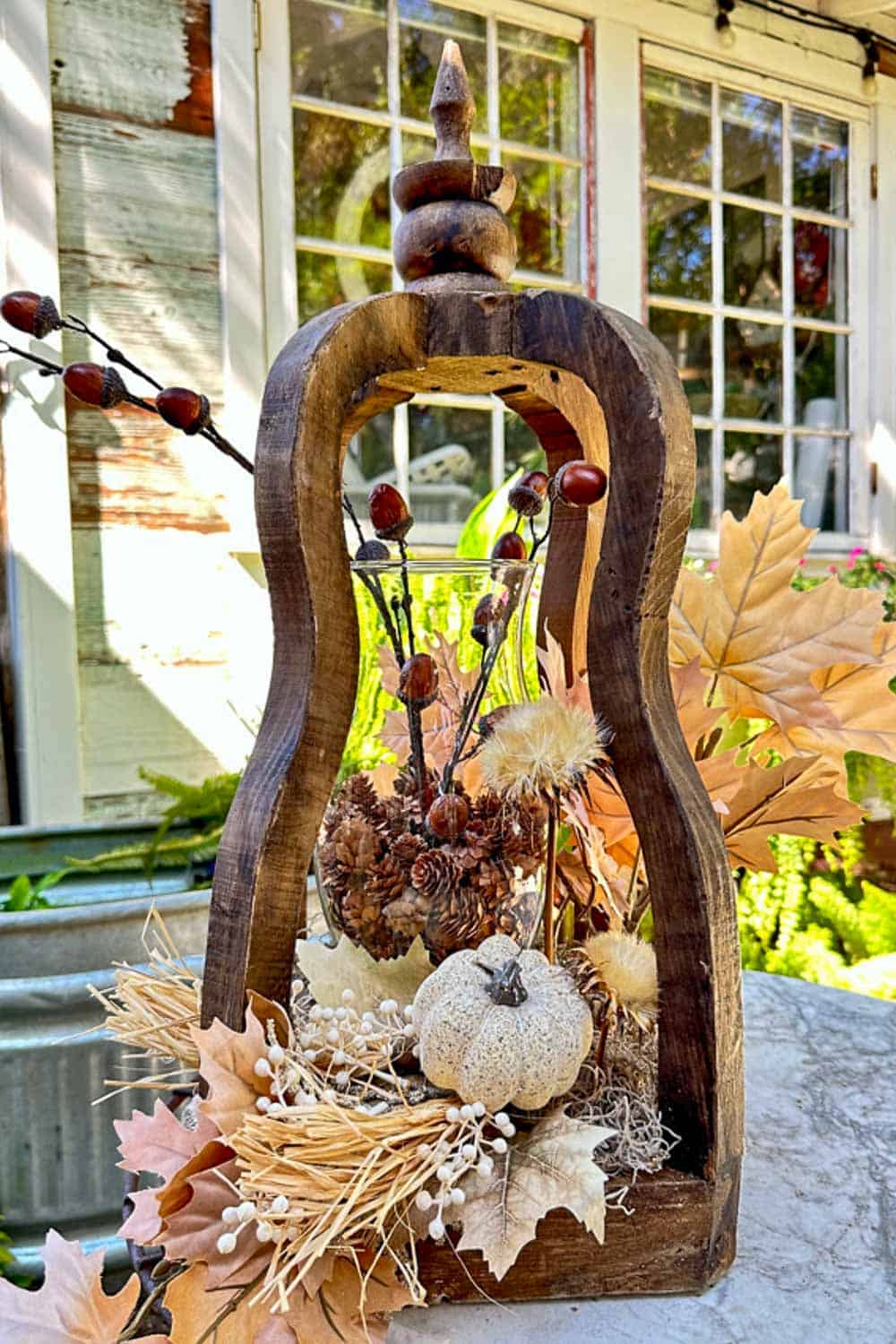 Glass hurricane fulled with small pine cones and stems of acorns in an open wooden lantern decorated with silk fall leaves.