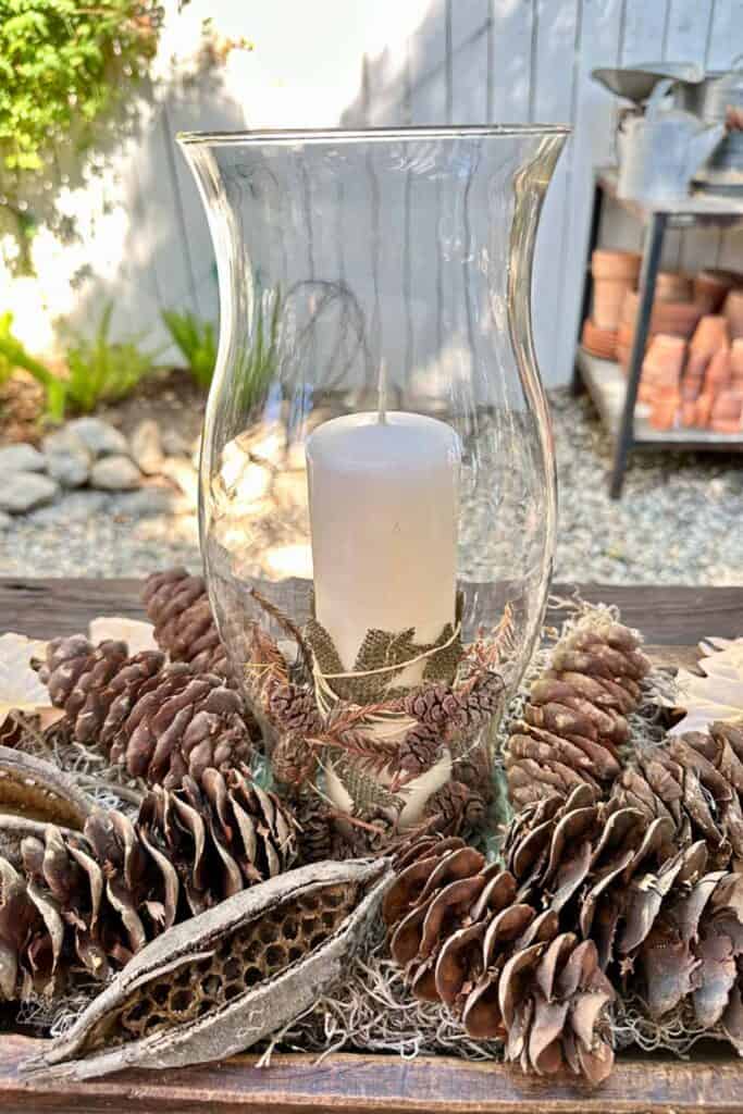 Simple fall arrangement with pine cones and a candle wrapped with leaves and small pine cones inside of a hurricane glass vase