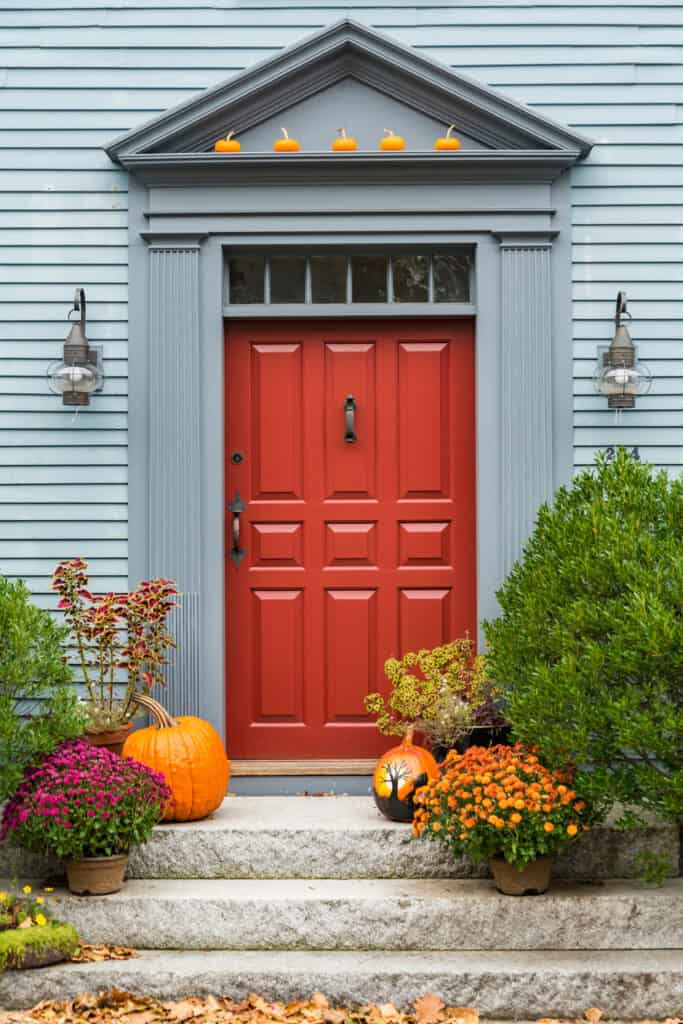 red front door on a blue house decorated for fall