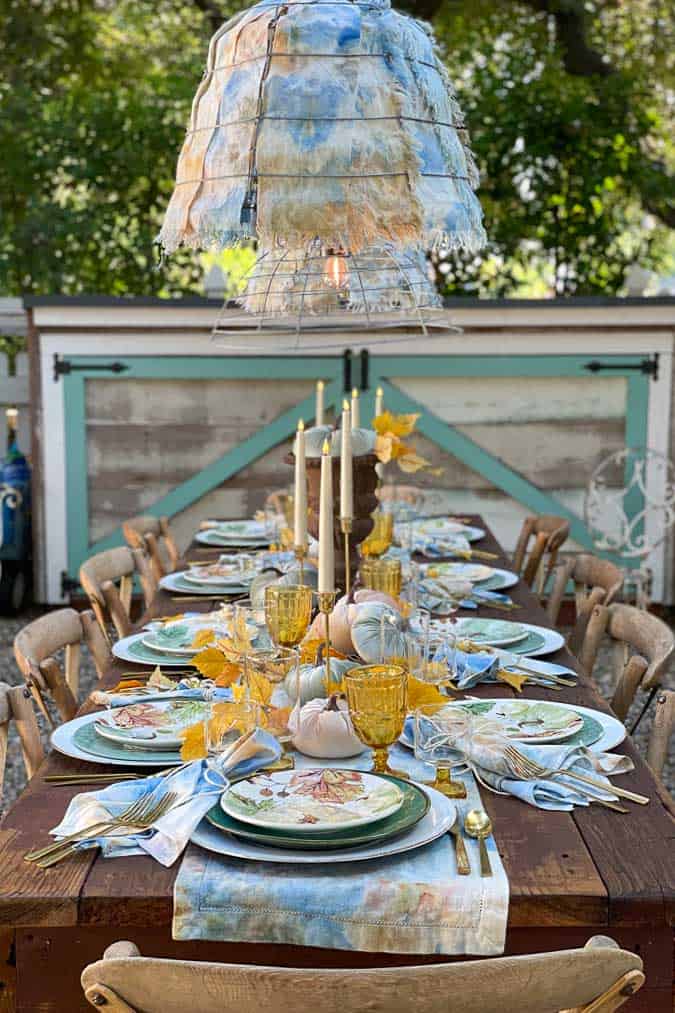 Outdoor tablescape in blue and gold with white candles, velvet pumpkins and beautiful linens. 