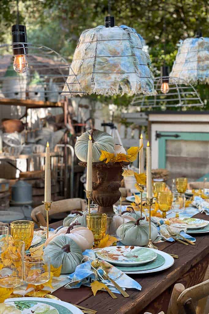 outdoor fall place setting with blue and gold color scheme and pumpkin centerpiece in a tall urn 