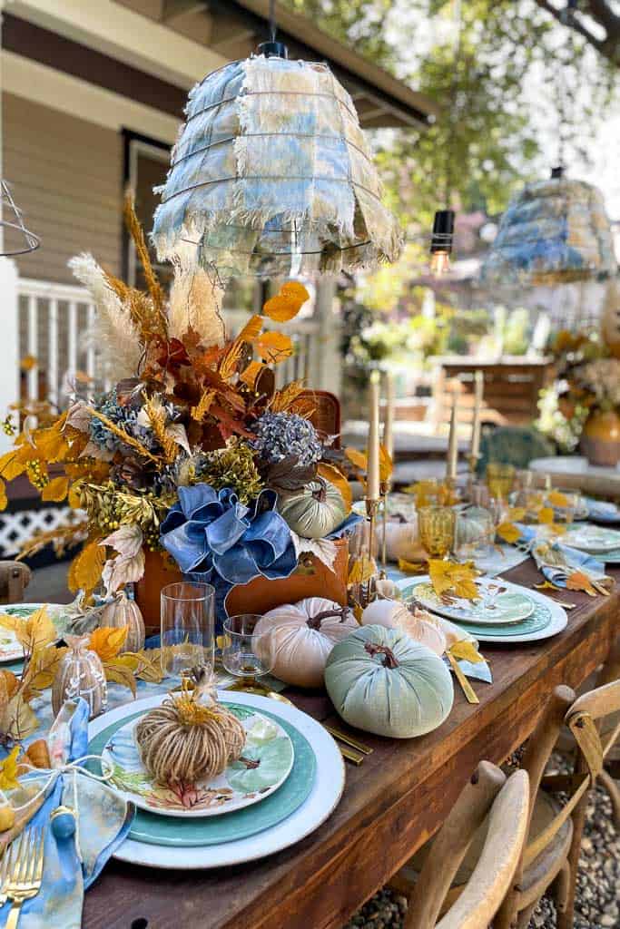 Outdoor tablescape in blue and gold with white candles, velvet pumpkins and beautiful linens
