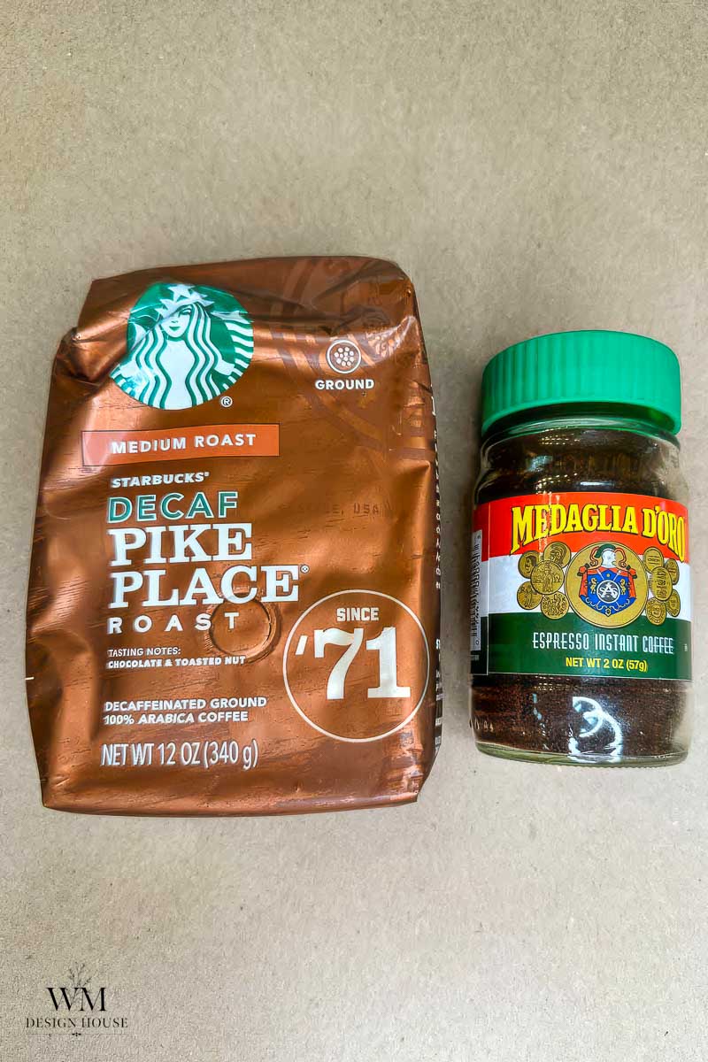 A bag of Starbucks Decaf Pike Place Roast coffee sits next to a jar of Medaglia D’Oro instant espresso coffee on a light brown surface, perfect companions for anyone curious about how to make coffee stained  paper.