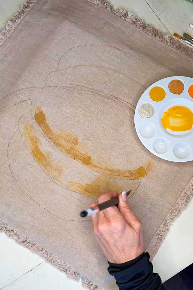 Hand painting a pumpkin onto a pillowcase.