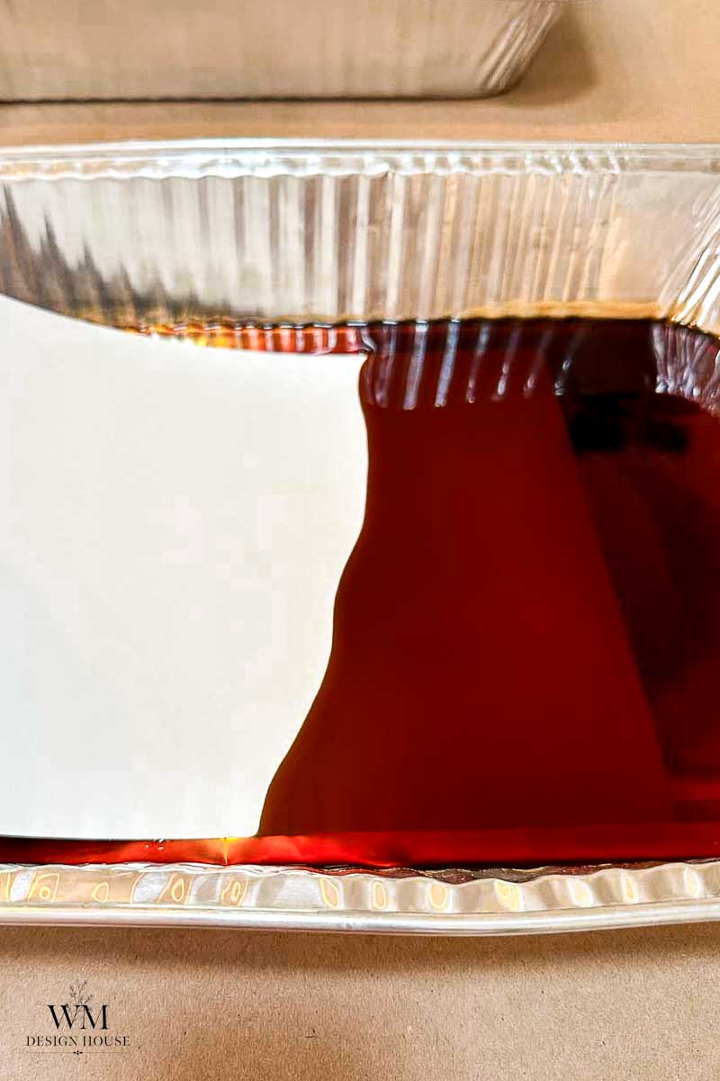 A close-up of a foil tray filled with dark coffee,  dipping ater color paper into the coffee to create  coffee stained paper.