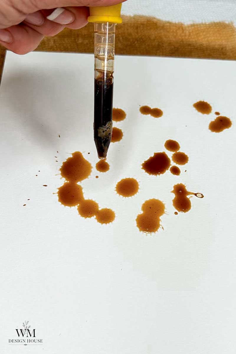 A hand holds a dropper above a white surface, releasing brown liquid droplets reminiscent of experiments in how to make coffee paper. Some droplets have splattered, creating irregular shapes. The WM Design House logo appears in the lower left corner.
