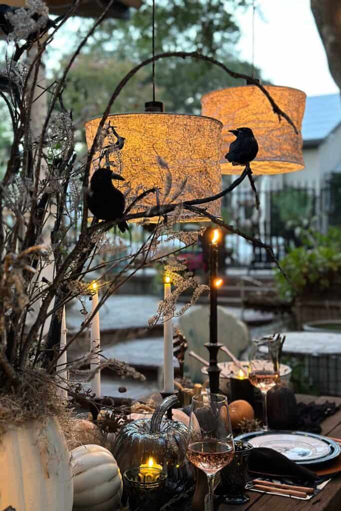Halloween tablescape with DIY lampshades illuminating the black crows and branches from the centerpiece on the table. 