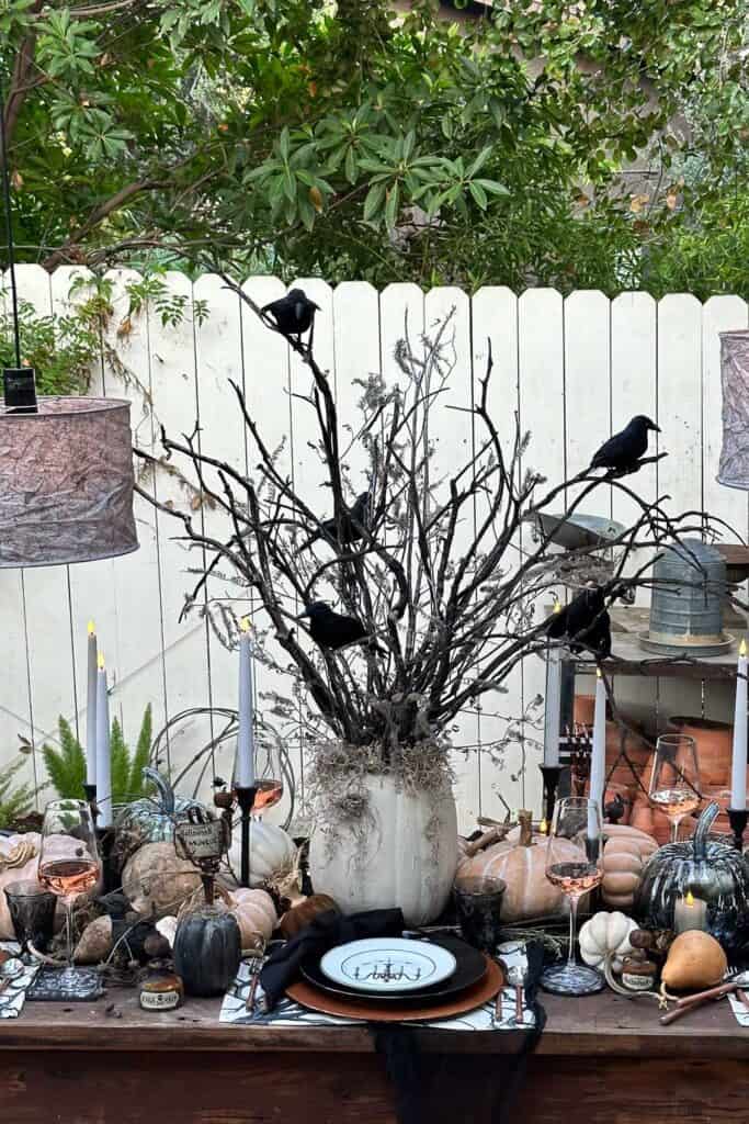 DIY Halloween tree made of charred branches in a white pumpkin vase with black crows hanging out in the limbs. 