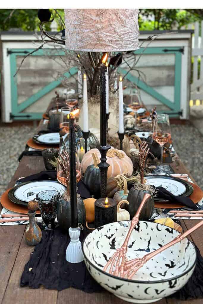 Halloween tablescape outside. The setting is a side yard with a a farm table set with black and white Halloween decorations for a spooktacular feast.