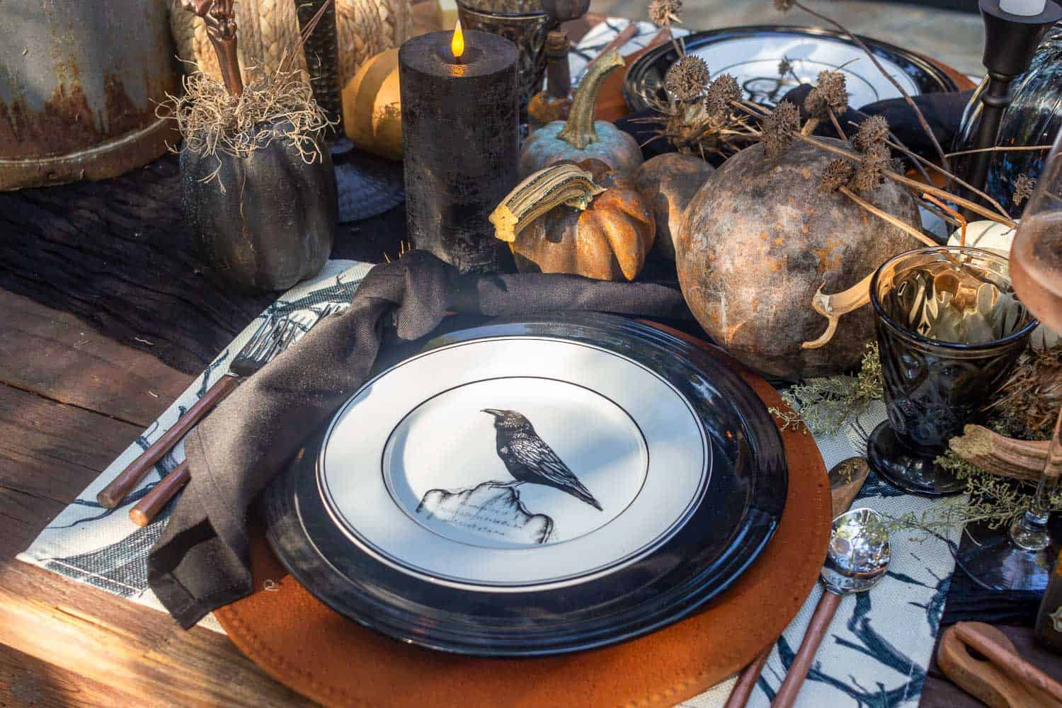 Halloween place setting with a cinnamon DIY charger, black pate, and a black and white salad plate—copper silverware to the sides and black and white crow placemats.