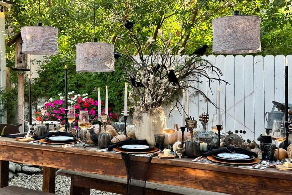 Halloween tablescape outside. The setting is a side yard with a a farm table set with black and white Halloween decorations for a spooktacular feast. 