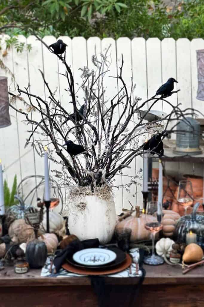 A Halloween centerpiece made out of burnt branches plastered into a pumpkin. Crows are sitting amongst the limbs.  