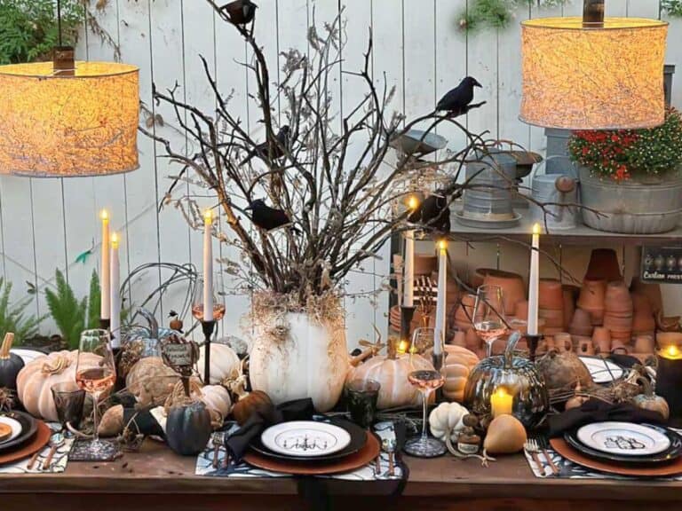 Halloween feature image of table with a centerpiece and dishes. A pumpkin filled with chared branches and crows, the table has pumpkins, gourds and beautiful Halloween dishes.