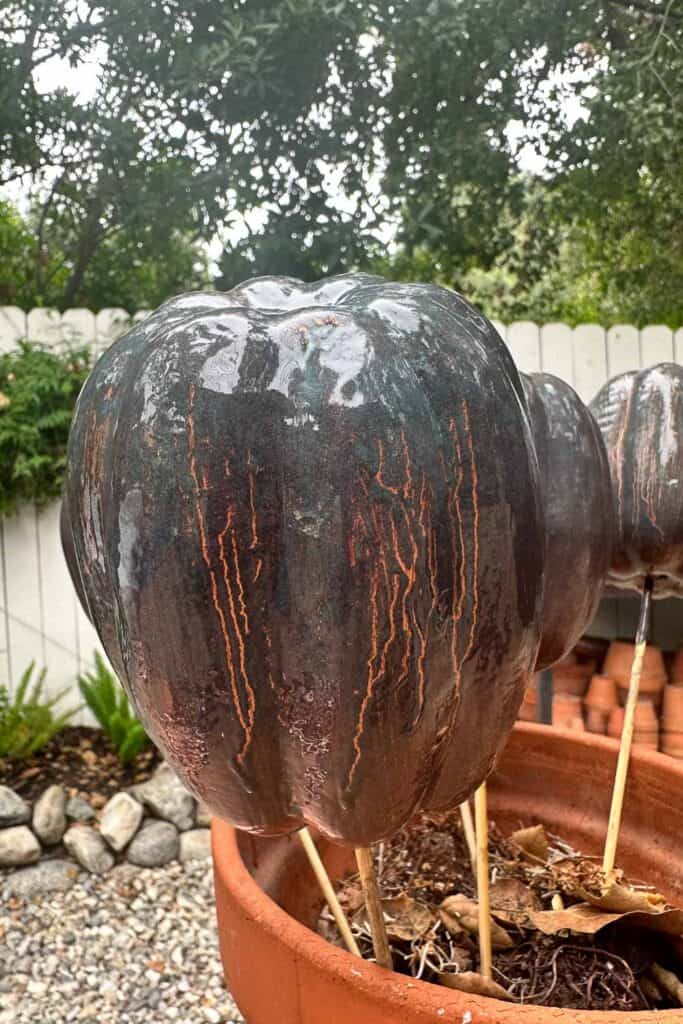 A faux pumpkin that has been painted and sprayed with a patina sitting in a pot to dry. 