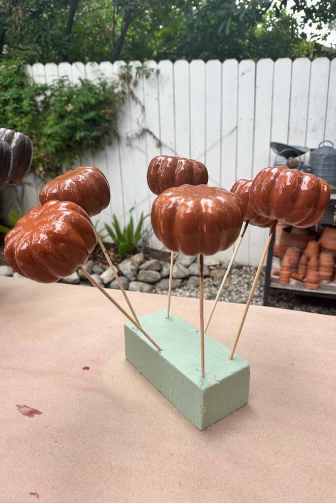Small pumpkins that have been painted with primer and the dowels inserted into a foam block to dry. 