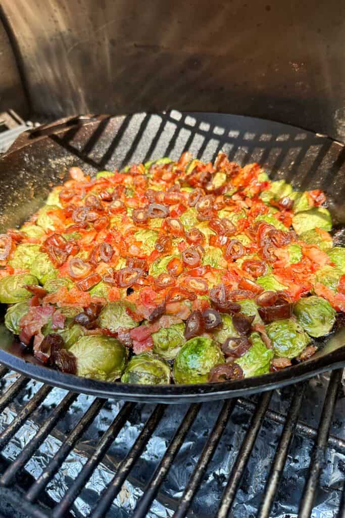 A Cast iron pan with the Brussels sprouts, bacon, and dates is placed in the smoker.