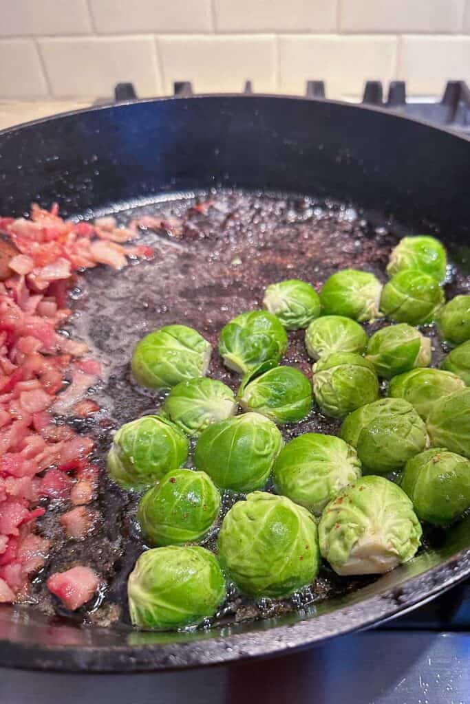 Bacon and Brussels sprouts frying in a cast iron pan.