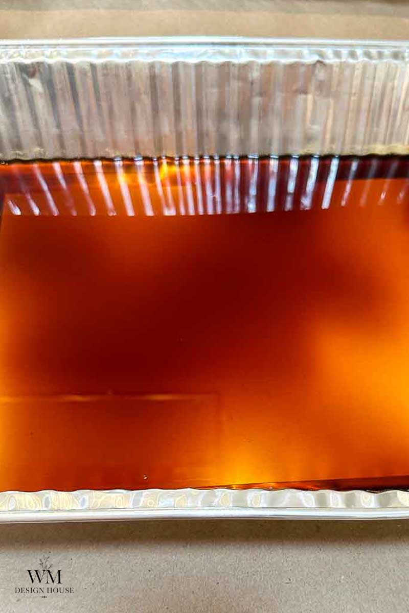 A close-up of a rectangular aluminum tray filled with a translucent amber liquid, reflecting light from above—an essential step in how to make coffee paper.