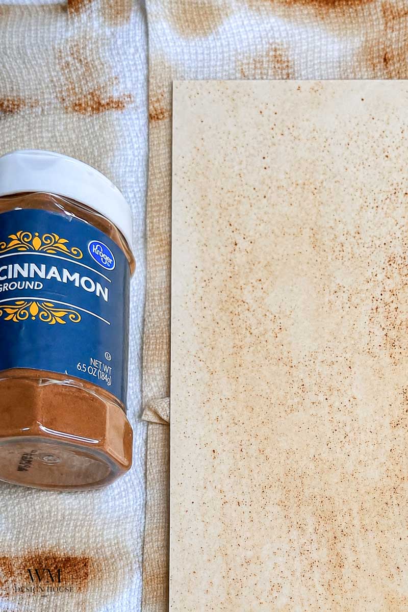 A container of ground cinnamon lies on a towel stained with cinnamon, next to a piece of paper speckled with cinnamon powder, perfect for experimenting with how to make coffee paper.