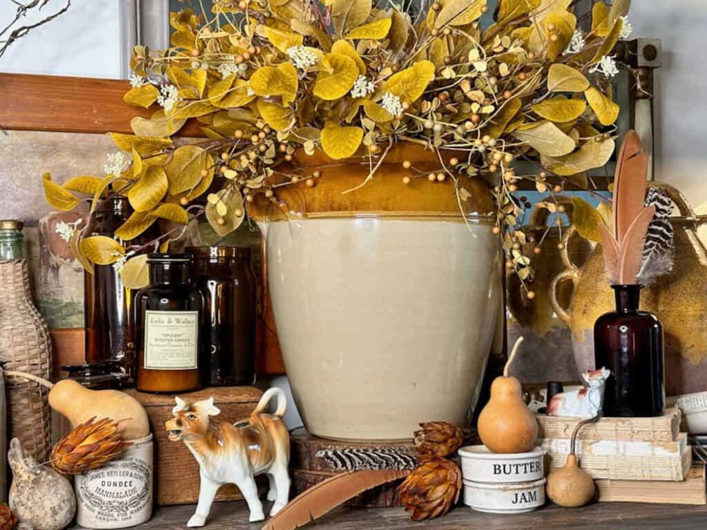 Fall vignette with crocks, gold berries, ceramic cows and old books to display for fall.