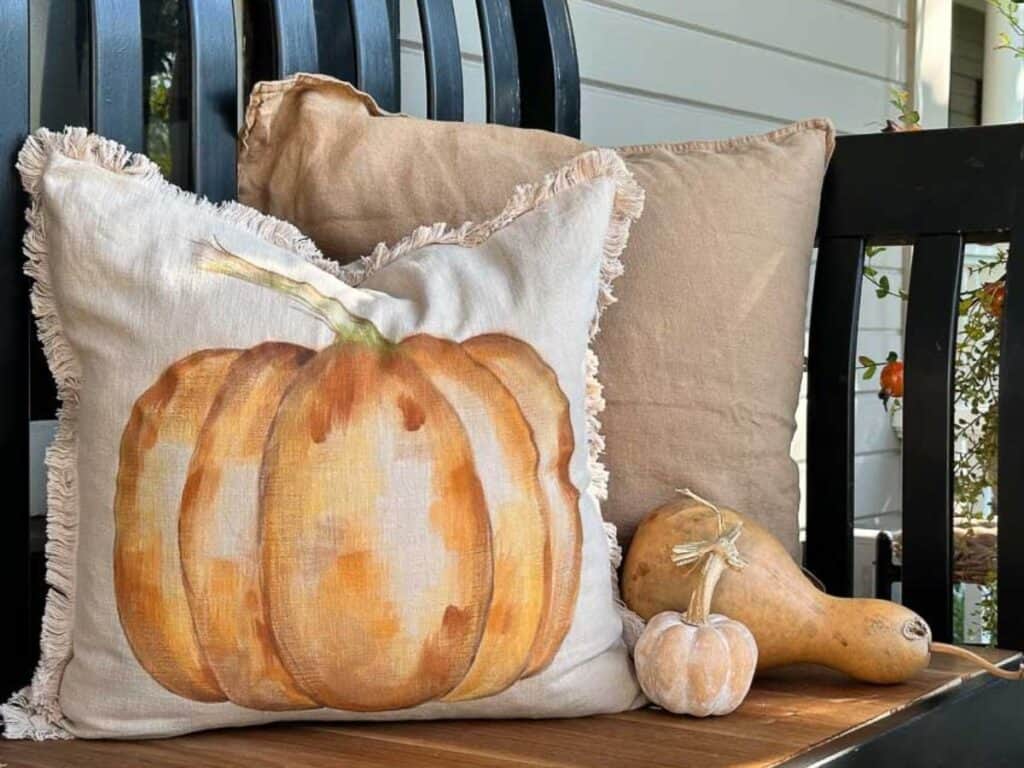 Painted pumpkin pillow sitting on a bench on the front porch.
