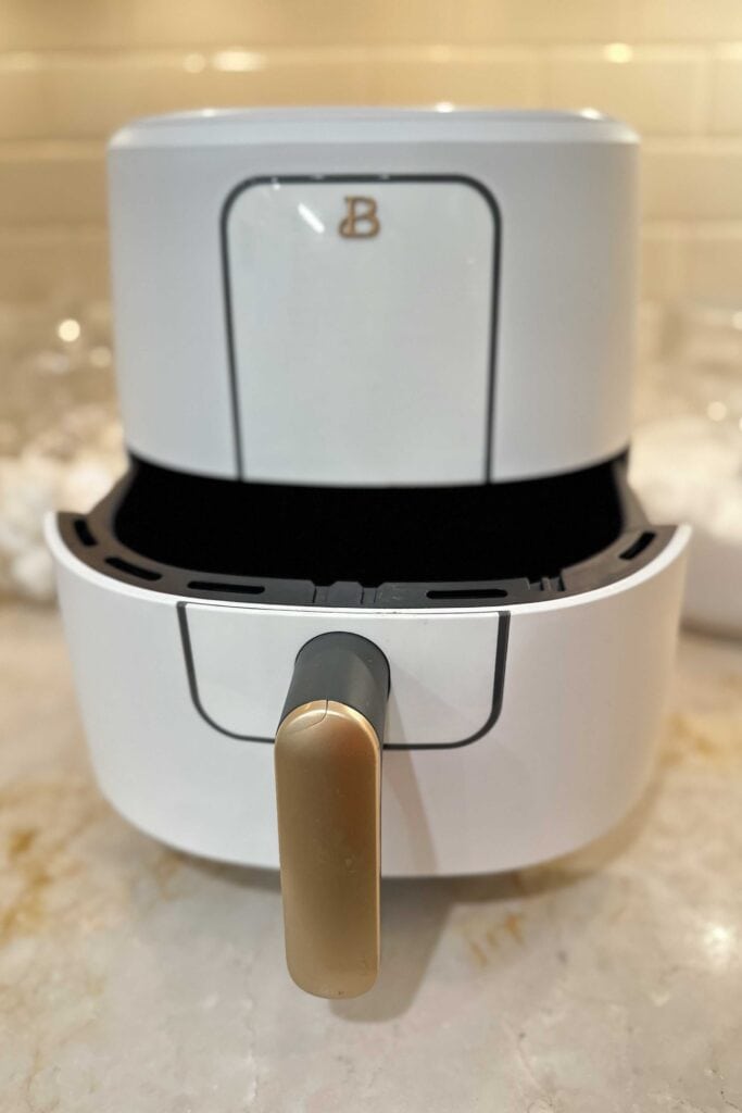 A white air fryer with the drawer open sitting on a kitchen counter.