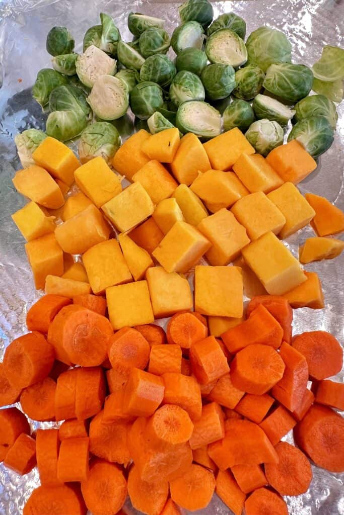 Fresh carrots, butternut squash, and brussels sprouts chopped in preparation for roasting.