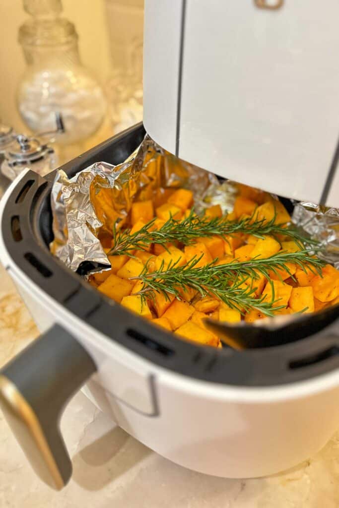 Butternut squash with fresh rosemary prepared for cooking in the air fryer basket.