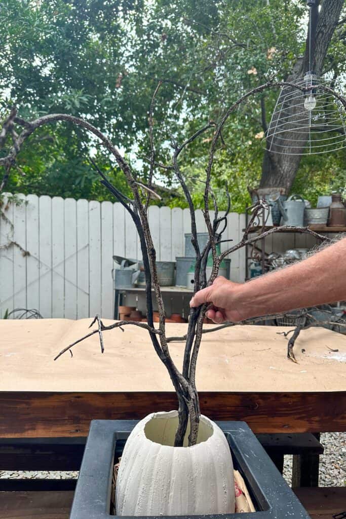 Placing branches in the pumpkin to create a DIY Halloween tree 