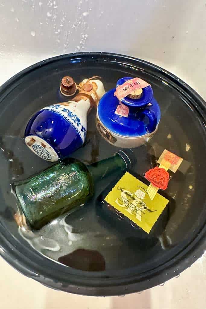 Five mini liquor bottles in a bath of water, removing labels and dirt. 