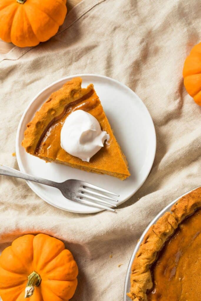 A slice of pumpkin pie on a white plate with a dollop of whipped cream.
