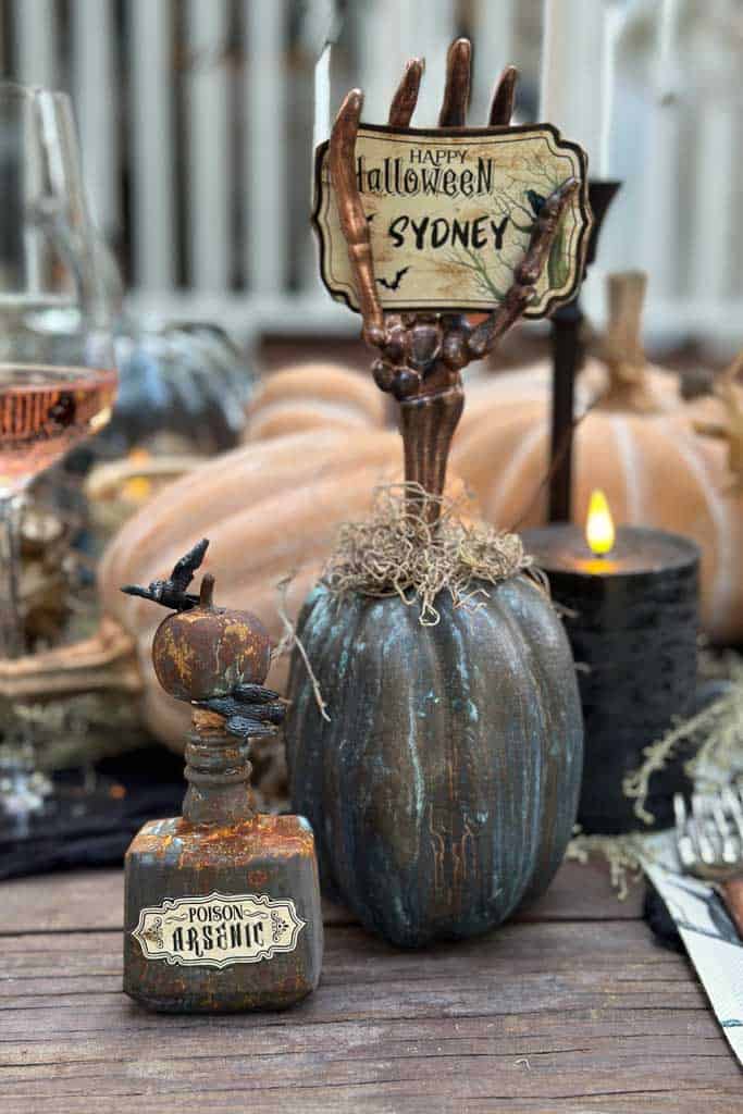 Patina pumpkin name card holder with a skeleton hand that has been painted holding a free printable name card.