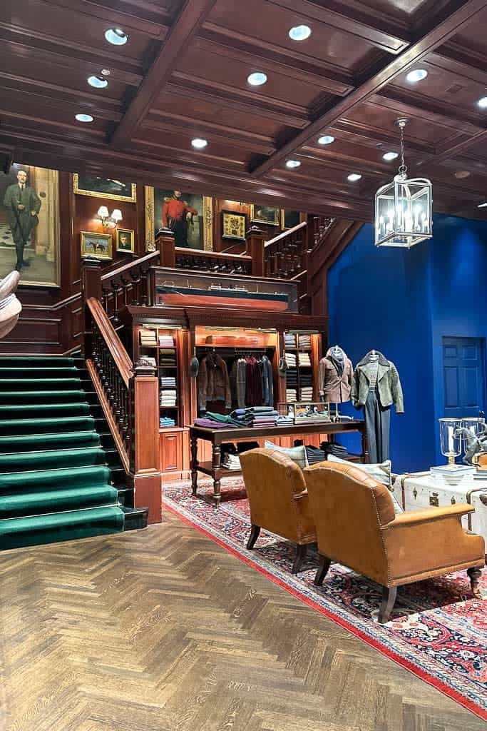 A Ralph Lauren room with dark wood, a staircase with green carpet and a blue wall. Decorated with dark wood tones and vintage finds. 