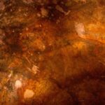 A close-up of a rusted, weathered metal surface with varying shades of brown, orange, and red, showcasing spots, scratches, and patches of corrosion that create a textured and abstract appearance with an intriguing rusty patina.