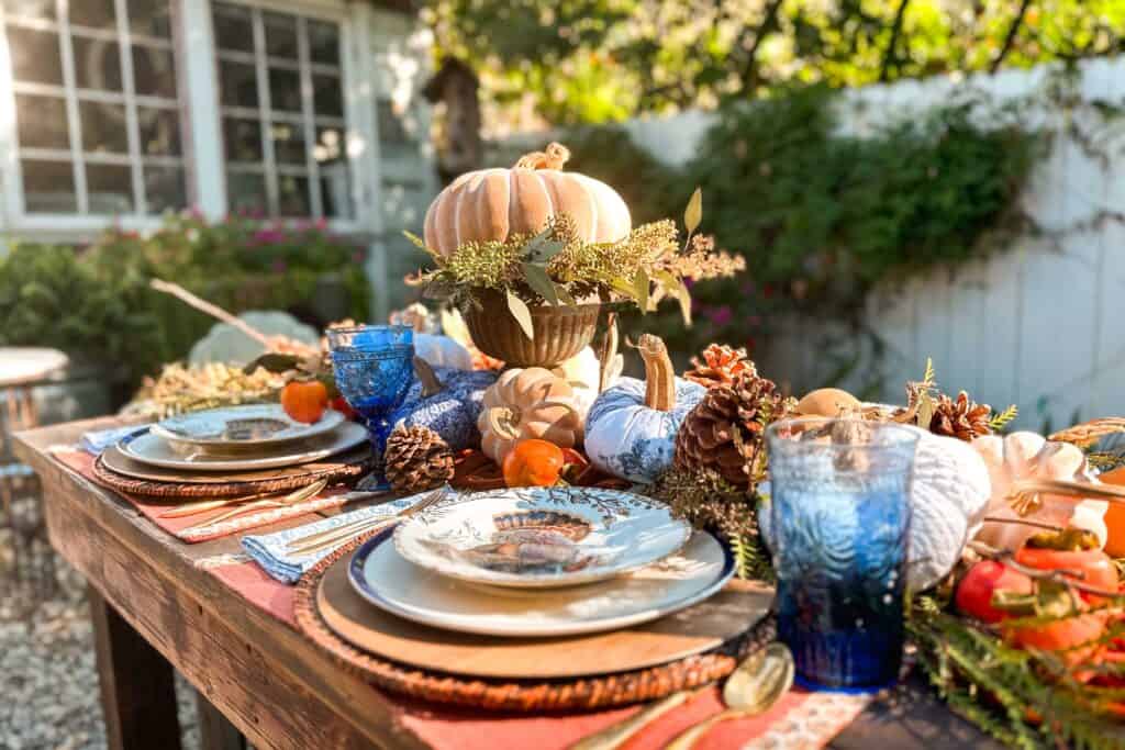 An orange and blue themed Thanksgiving table with pumpkins, persimmons, and fresh greenery.-Blue and Orange Thanksgiving Table Decor Ideas
