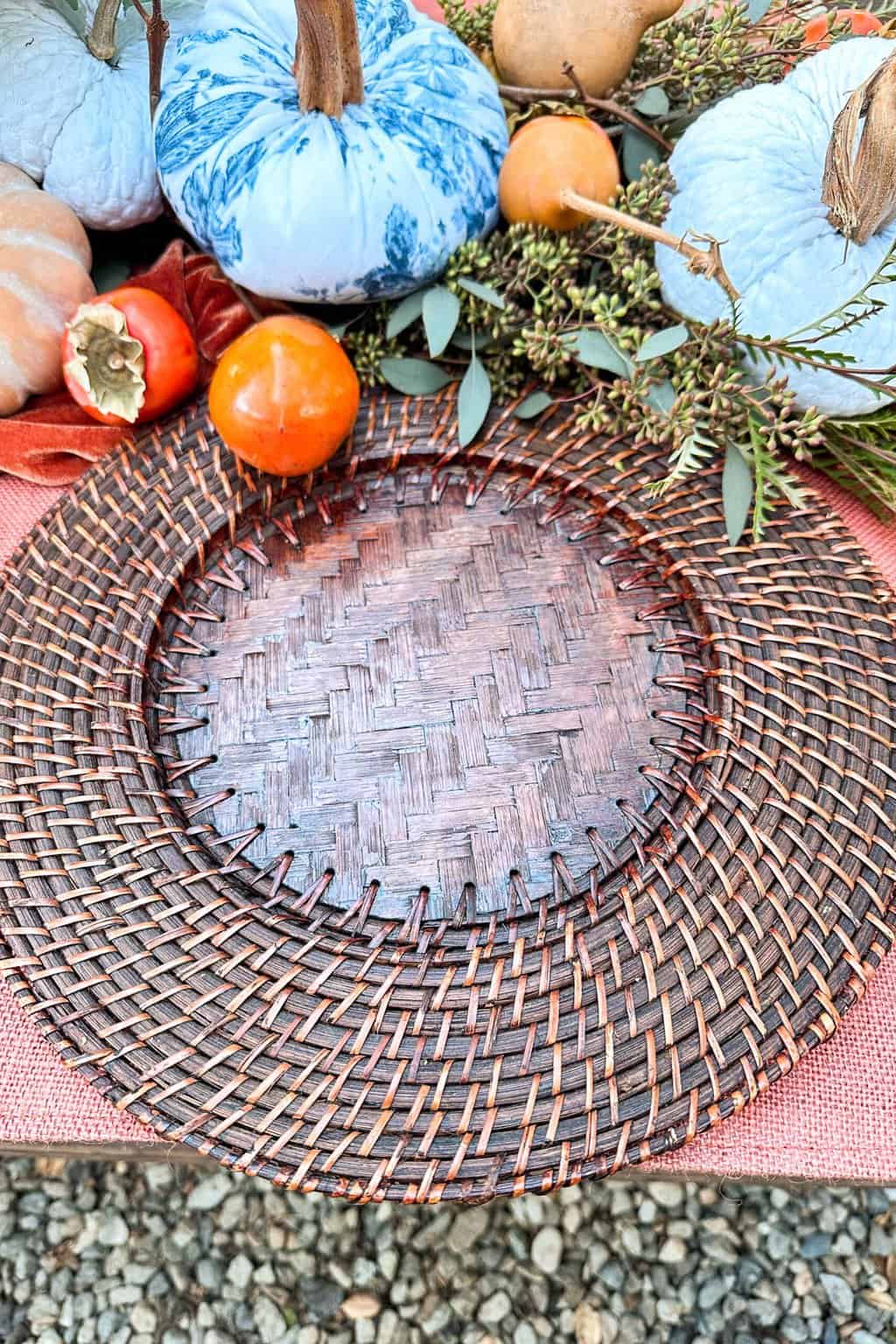 Table setting in progress with two chargers sitting on a table decorated with persimmons and blue and white pumpkins.