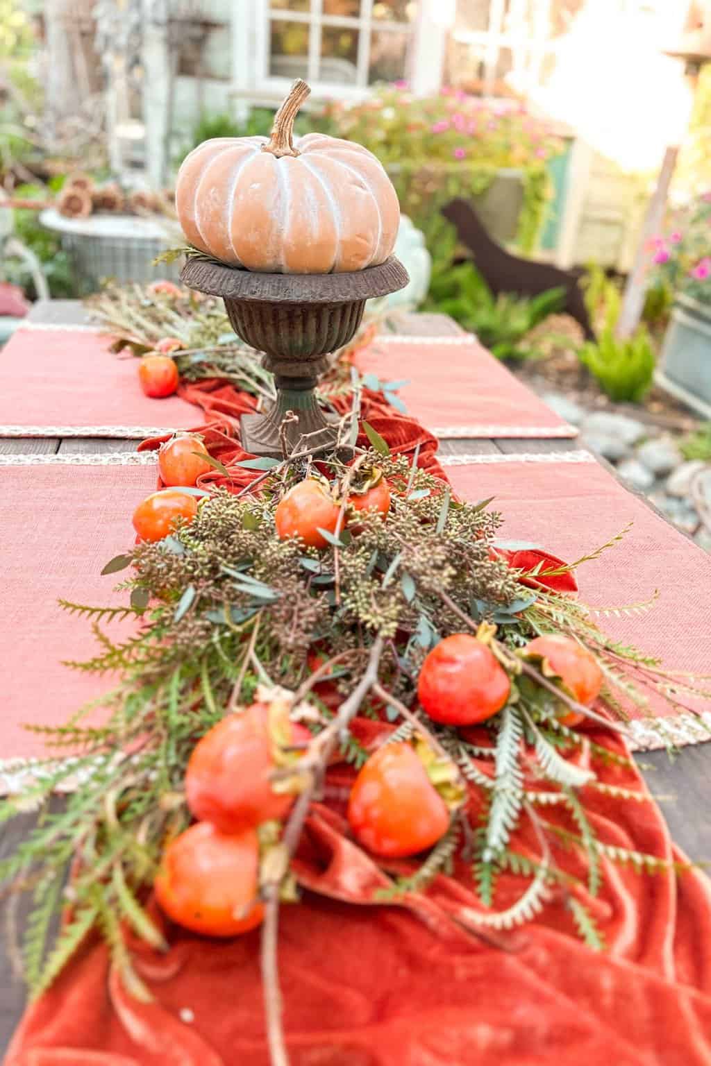 Table setting in process with placemats, table runner, greenery, fruit, and a centerpiece with a pumpkin