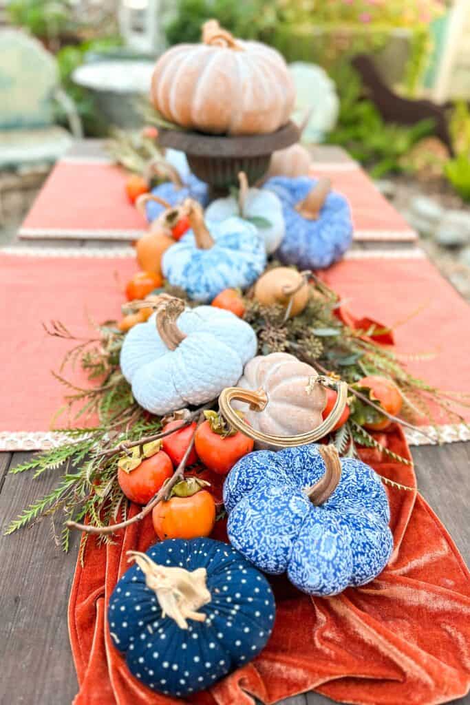 Blue and Orange Thanksgiving Table Decor Ideas-Blue and white pumpkins sitting amongst fresh greenery and persimmons on the Thanksgiving table.